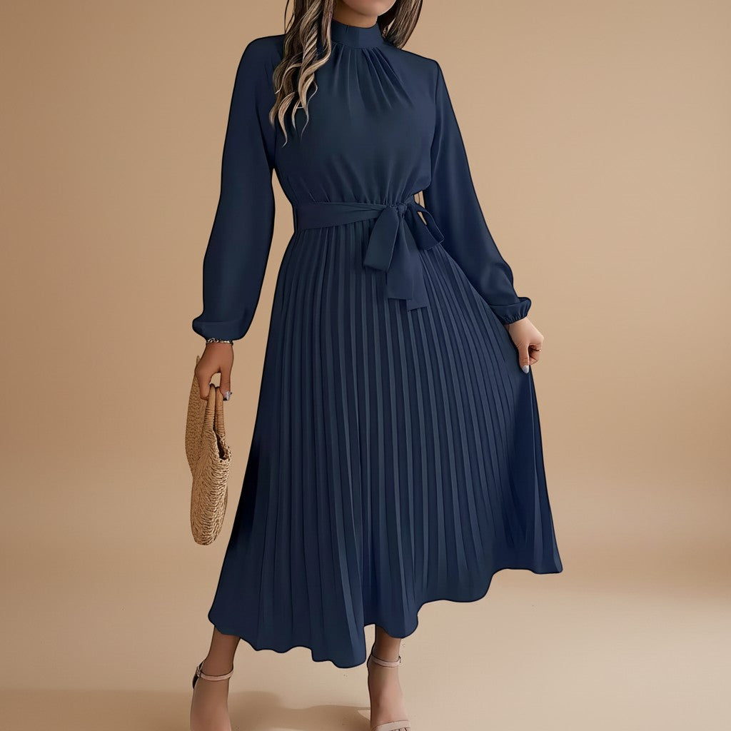 Yemelia navy blue long sleeve pleated midi dress with high neck and waist tie. Elegant, flowing silhouette.